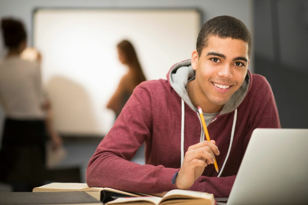 A handsome man with a pencil and lovely smile studying in front of his books and laptop